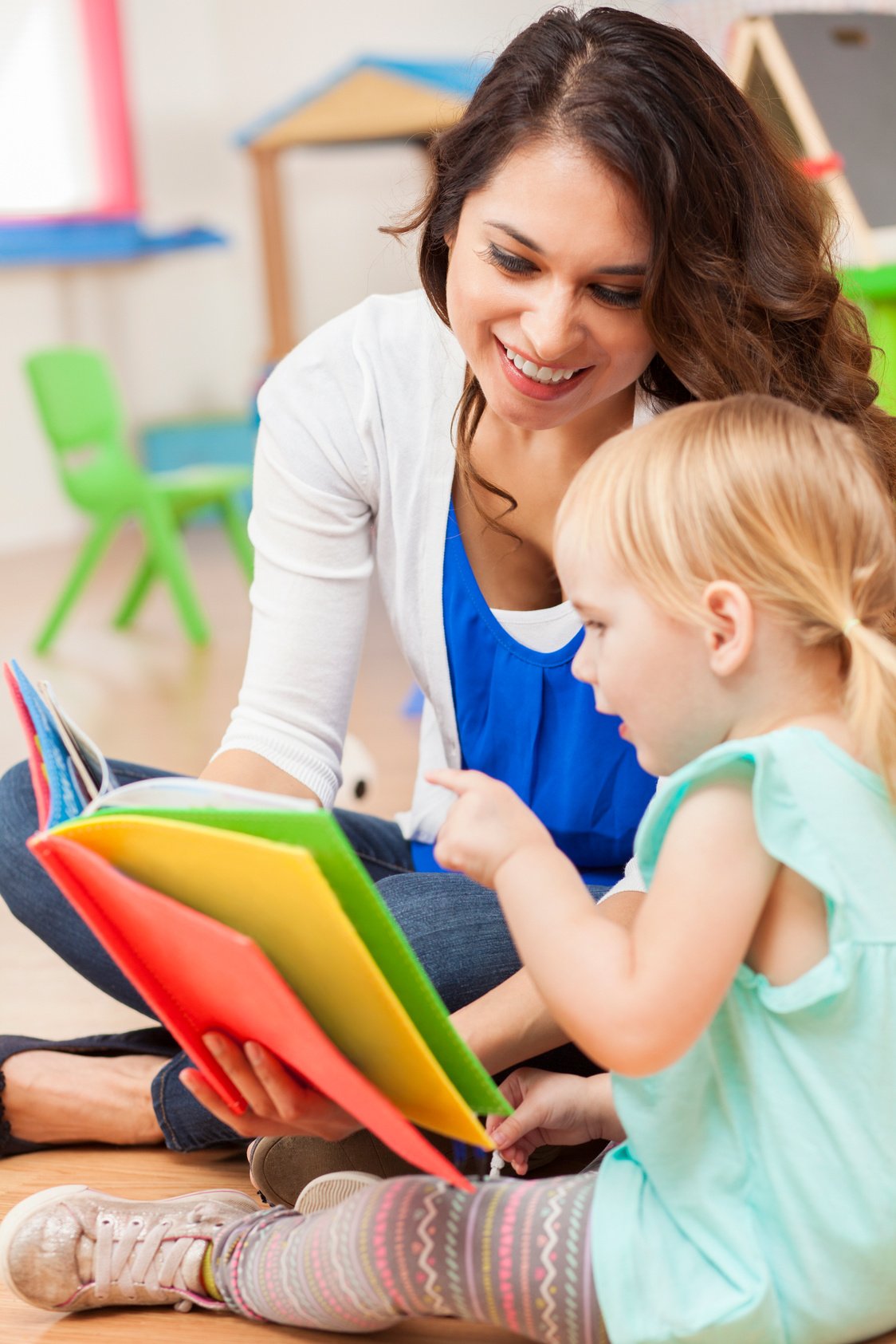 Daycare teacher reading to cute toddler girl